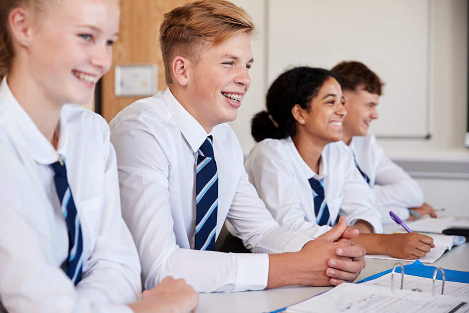 Four secondary school pupils smiling in a classroom setting.