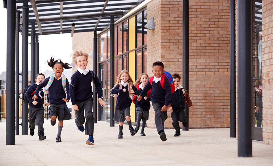 A group of primary school children running outside a school.